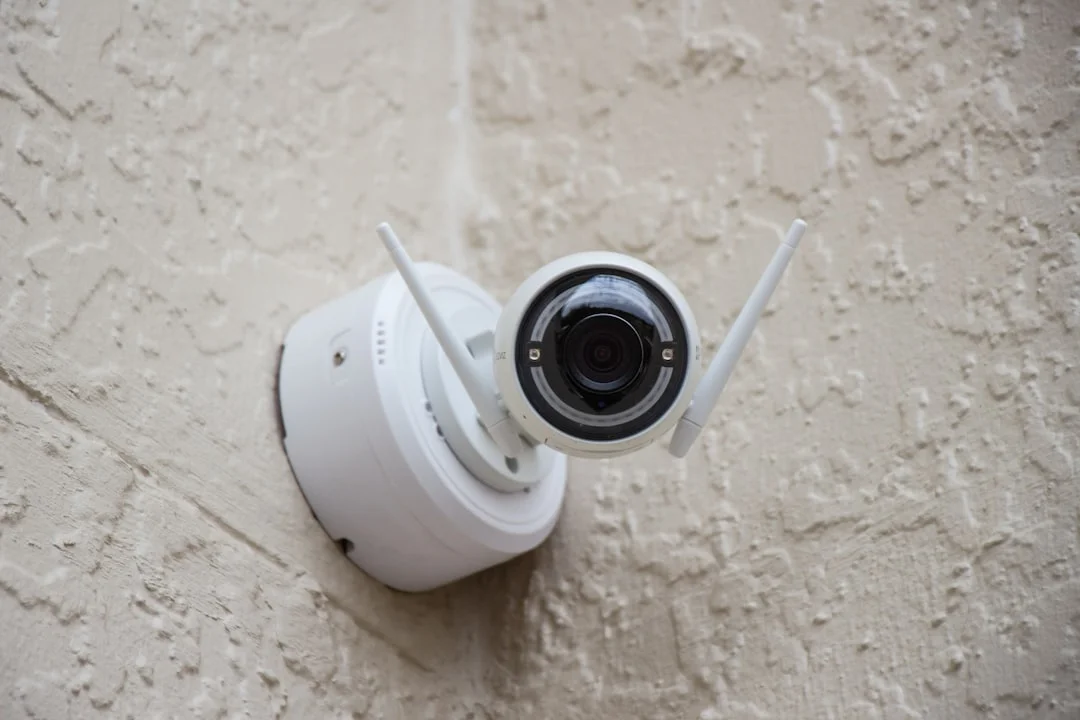 A wall-mounted 4K PoE IP camera overlooking a small business parking lot at dusk, with a laptop open to a VMS live-view dashboard in the foreground